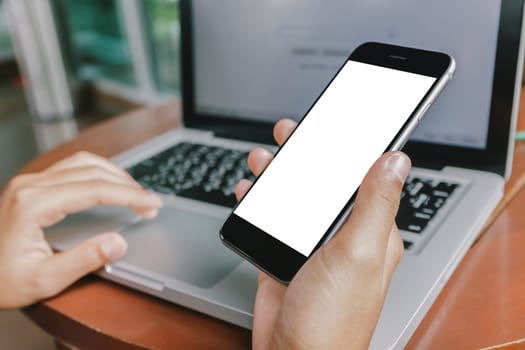 hand holding phone and using laptop computer in coffee shop