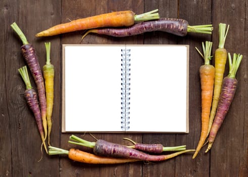 Fresh organic rainbow carrots with Recipes book on a wooden table