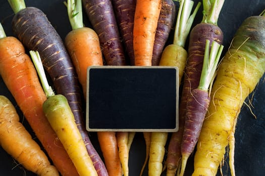 Fresh organic rainbow carrots and a small chalkboard on wood
