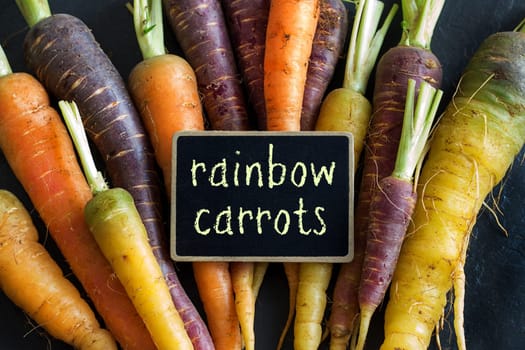 Fresh organic rainbow carrots and a small chalkboard on wood