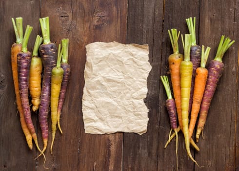 Fresh organic rainbow carrots and craft paper on wood