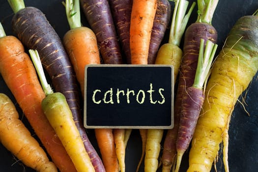 Fresh organic rainbow carrots and a small chalkboard on wood