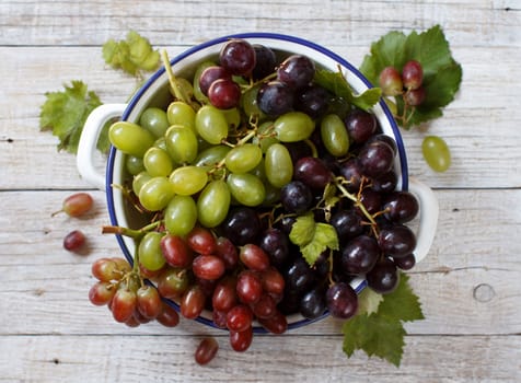 White, red and blue grapes in a bowl on wooden table