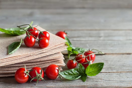 Raw lasagna sheets,basil and cherry tomatoes on a wooden table