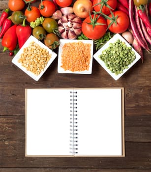 Legumes in bowls, vegetables and notebook on a wooden table