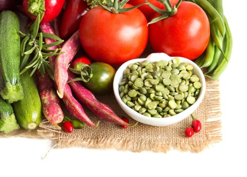 Green peas in a bowl and vegetables on a white background