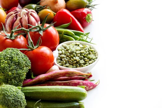 Green peas in a bowl and vegetables on a white background