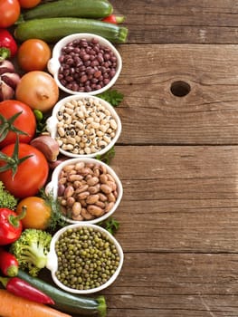 Legumes in bowls and vegetables on a wooden table