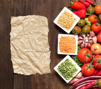 Legumes in bowls, vegetables and paper on a wooden table