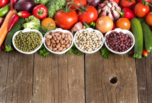 Legumes in bowls and vegetables on a wooden table