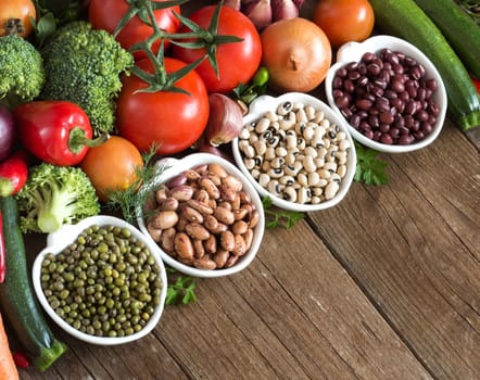 Legumes in bowls and vegetables on a wooden table