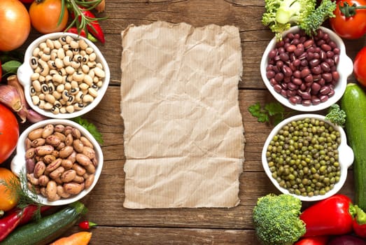 Legumes in bowls and vegetables on a wooden table