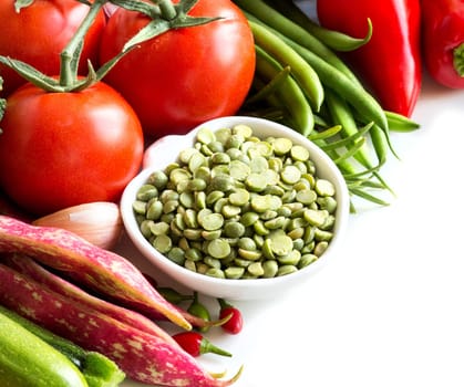 Green peas in a bowl and vegetables on a white background
