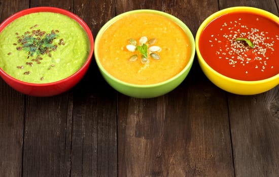 Tomatoe, pumpkin and green peas soups on a wooden table