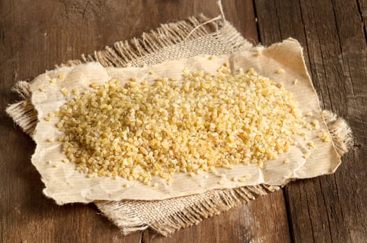 Raw bulgur on a paper and burlap on a wooden table