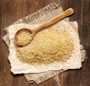 Raw bulgur with a spoon on a wooden table