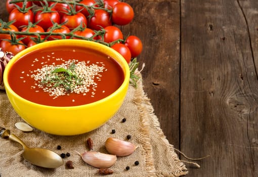 Fresh tomatoes soup with vegetables and spoon on a wooden table