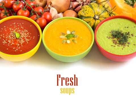 Three fresh soups in colorful bowls and vegetables