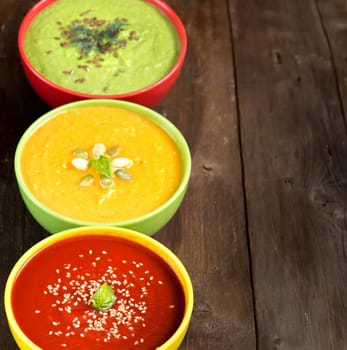 Tomatoe, pumpkin and green peas soups on a wooden table