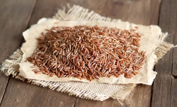 Red rice on burlap and paper on a wooden table