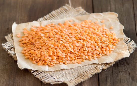 Red lentils in paper and burlap on a wooden table