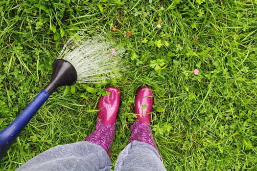 A woman with rubber boots waters the lawn with a watering can