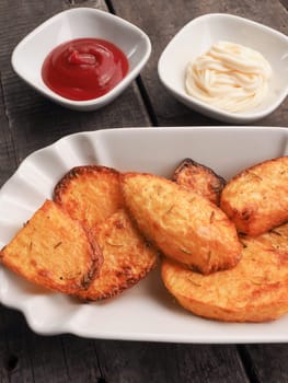Rosemary potatoes with ketchup and mayonnaise on an old wooden kitchen table