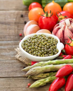 Mung beans in a bowl and vegetables on wooden table
