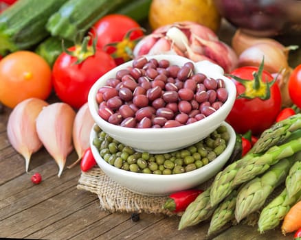 Mung and azuki beans in a bowl and vegetables on wooden table