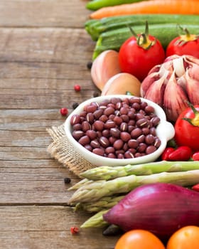 Azuki beans in a bowl and vegetables on wooden table