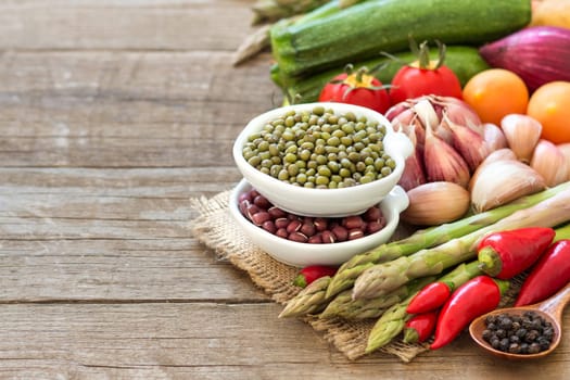 Mung and azuki beans in a bowl and vegetables on wooden table