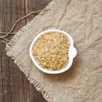 Raw unpolished rice in a bowl on burlap