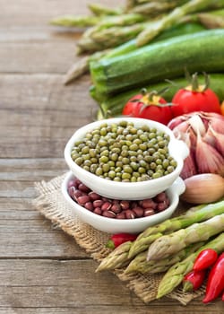 Mung and azuki beans in a bowl and vegetables on wooden table