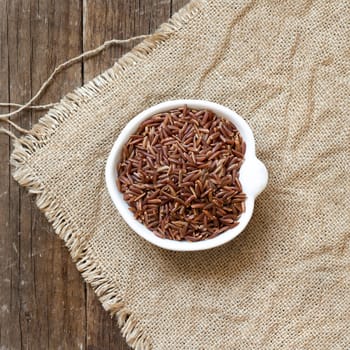 Raw red rice in a bowl on burlap