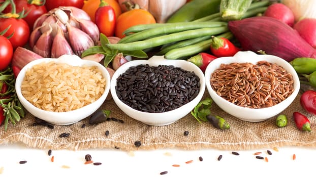 Red, black and unpolished organic rice in bowls and vegetables