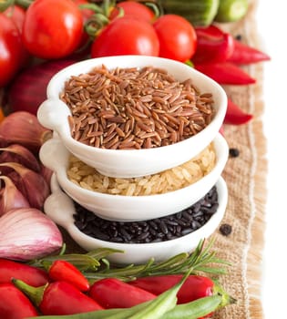 Red, black and unpolished organic rice in bowls and vegetables