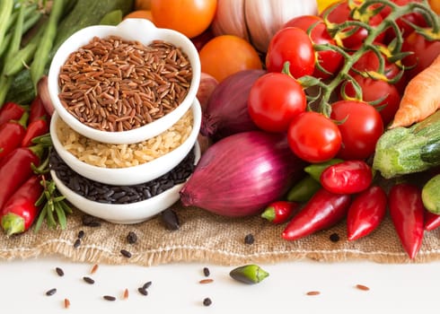 Red, black and unpolished organic rice in bowls and vegetables