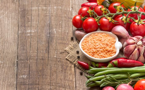 Red lentils in bowl and vegetables on a wooden table