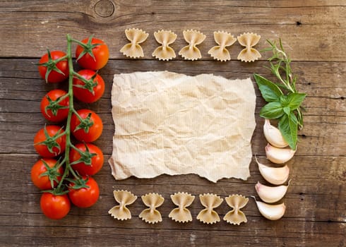 Pasta, tomatoes, garlic, herbs and paper on wooden background