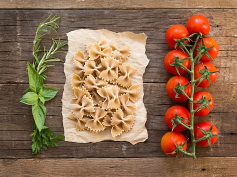 Pasta, tomatoes and herbs on wooden background