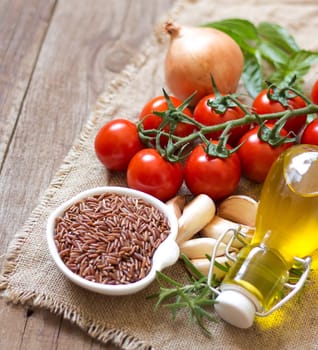 Organic red rice, tomatoes, olive oil, garlic and herbs on wooden background
