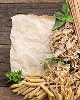 Pasta, herbs and paper on wooden background