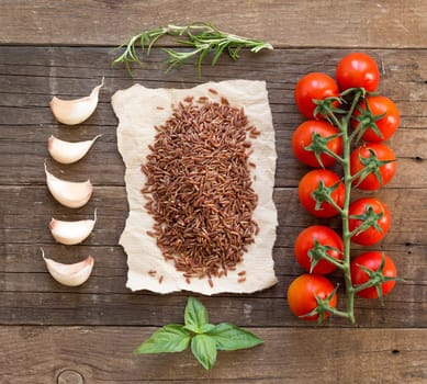 Organic red rice, tomatoes, garlic and herbs on wooden background