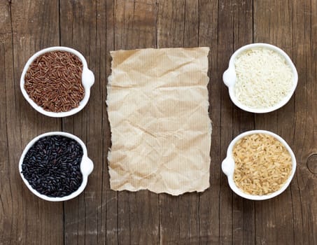 Variety of rice in bowls on wooden table and old paper