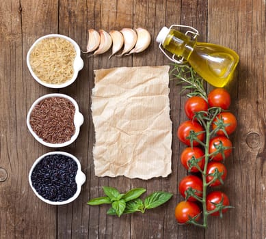 Variety of rice in bowls, olive oil, herbs and vegetables on wooden table and old paper