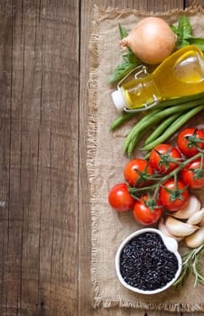 Black organic rice, vegetables and herbs on wooden background