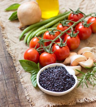 Black organic rice, vegetables and herbs on wooden background