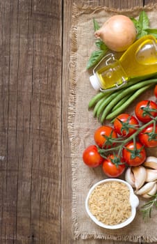 Whole unpolished organic rice, olive oil, vegetables and herbs on wooden background