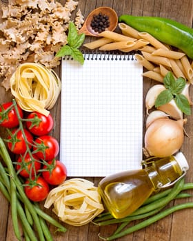 Pasta, vegetables, herbs and notebook on old wooden table