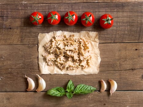 Pasta, tomatoes, garlic and basil on wooden background